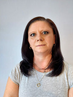 Ewa Pląsek. Szare tło, długie ciemne włosy. Postać w szarej koszulce.