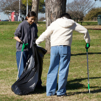 A pair of volunteers help each other hold a trash bag open.