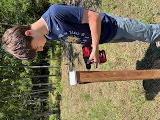 Eagle Scout fixes wayfinding arrows to posts using a drill.