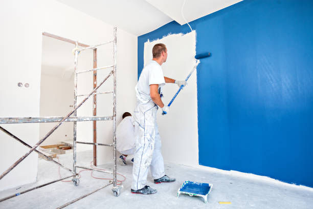 Painters applying white paint on blue interior wall.