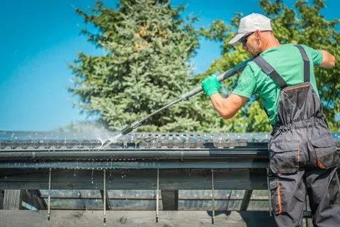 Worker cleaning house gutters with a pressure washer.