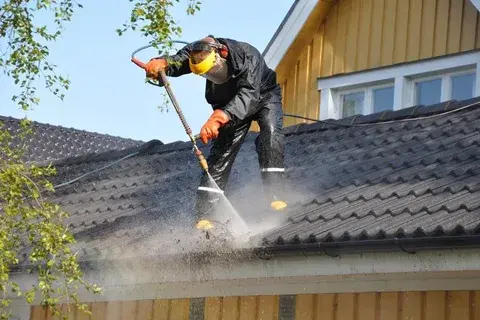 Worker pressure washing a tiled roof.
