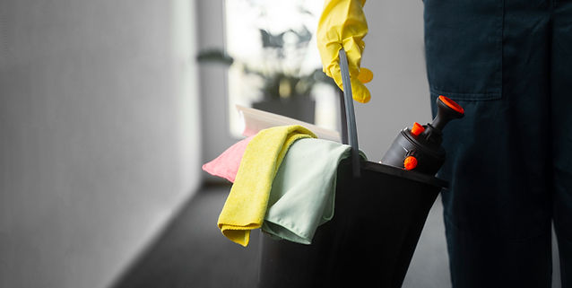 Person in yellow gloves holding a black bucket with cleaning supplies and cloths.