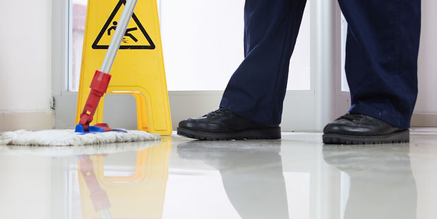 Person mopping a shiny floor near a caution sign for janitorial services.