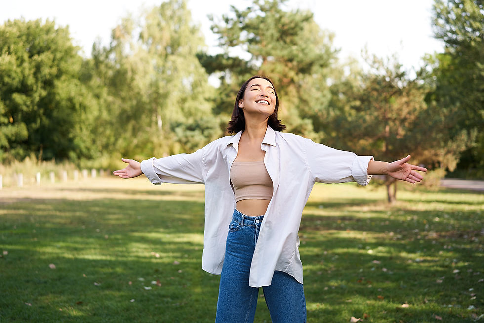 Carefree Asian girl laughing and dancing in a sunny park, raising her hands in joy on a beautiful summer day.