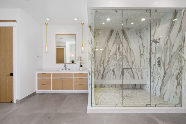 Modern bathroom with Calacatta Gold Marble shower enclosure, light wood vanity, and gray tile floor