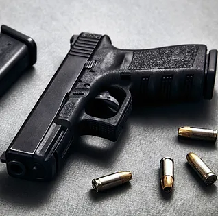 Close-up of black handgun on gray surface with bullets scattered nearby