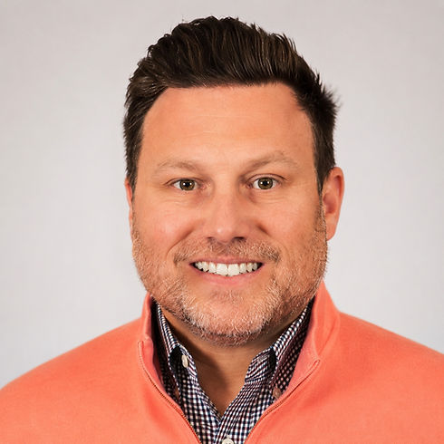 Man with short dark hair and beard, wearing an orange sweater over a checkered shirt.
