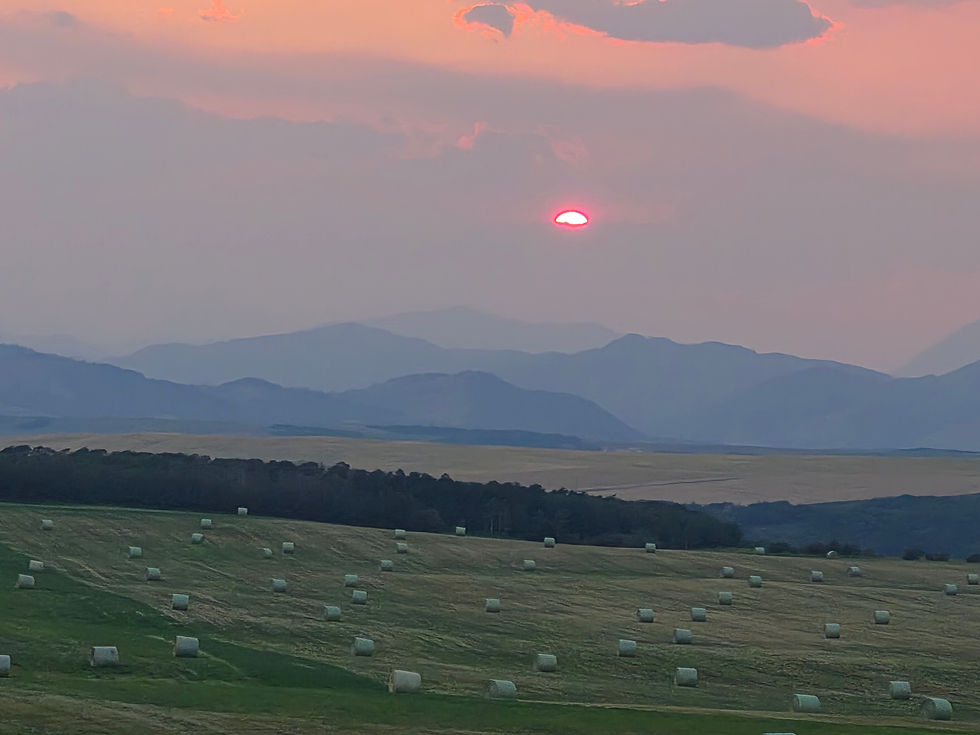 Sunset over the mountains with a field of hay bales.
