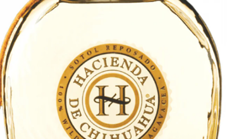 Bottle of Sotol Reposado with a wooden cap, labeled "Hacienda de Chihuahua." Clear liquid inside, 750ml. Elegant and artisanal design.