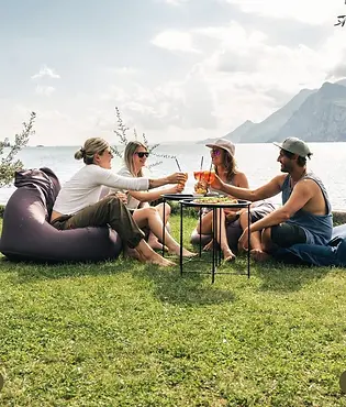 Vier Personen stoßen mit Aperol Spritz am Gardasee Ufer an