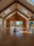 Interior view of Yoga at The Grange studio facing towards the patio windows. Three yoga mats are laid out on the wooden floor with bricks, blocks, blankets and eye pillows.