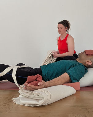 Yoga teacher assisting a student in restorative reclined butterfly shape.
