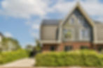 Moderne Nederlandse woning met zonnepanelen, donkere gevelbekleding en rode bakstenen, omgeven door groen.