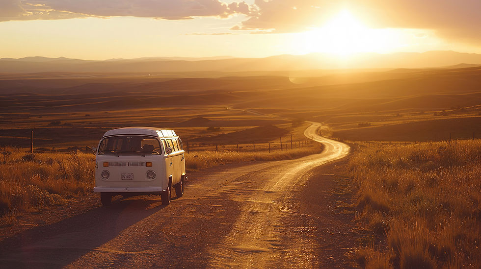 Witte Volkswagen T2 bus rijdt bij zonsondergang over een onverharde weg door een open, goudgeel gekleurde landschap.