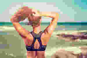 athletic girl ties hair in sports bra on beach