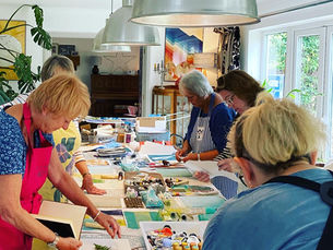 Women around a long table making gel plate prints with artist Caroline Houchell at a workshop.
