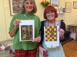 Two ladies proudly holding their reduction lino prints made at a workshop with Sue Welfare