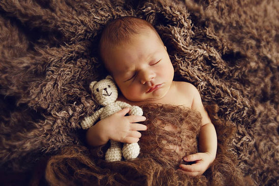 Neugeborenes in brauner flauschiger Decke mit Teddybär im Arm.