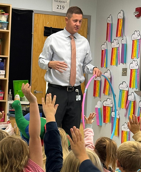 Character Counts coach leading a classroom lesson as students sit on the floor and raise their hands to participate.