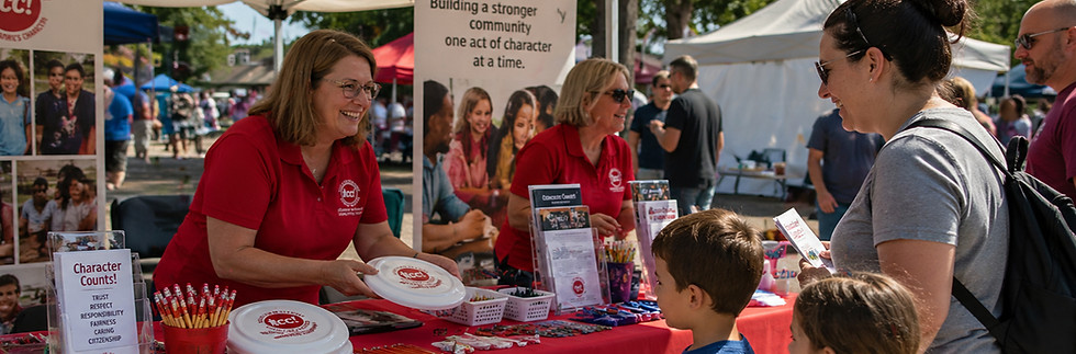 Character Counts volunteers at a community event table with red branded tablecloth, sharing materials and interacting with families and children.