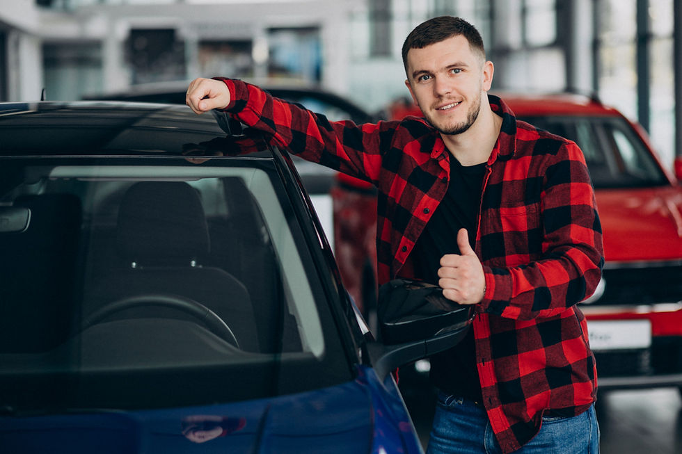 Smiling man leaning on a car with thumbs up in a showroom.