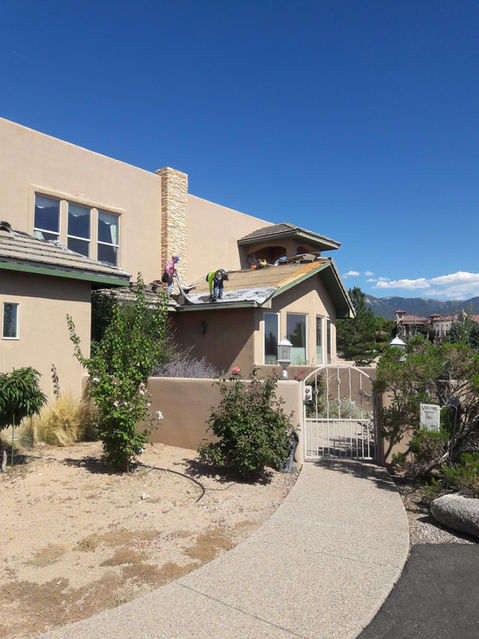 Roofers working on a residential roof with a clear blue sky above.