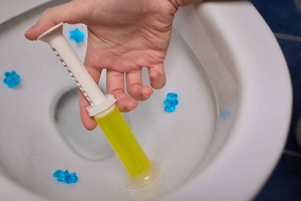 Hand holding yellow cleaning gel dispenser inside a toilet bowl with blue flower-shaped fresheners. White and blue background.