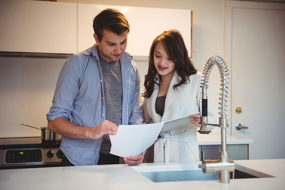 Young couple reviews papers together in a bright kitchen by the sink, with a modern faucet and a pot on the stove.