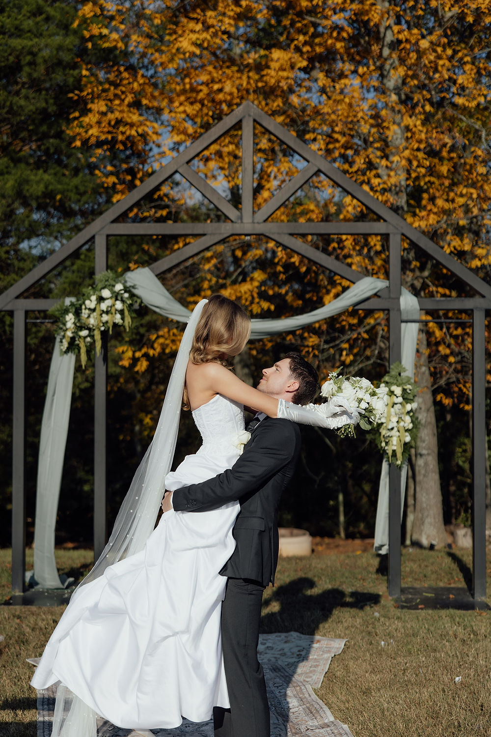 Groom holds bride at wedding arch