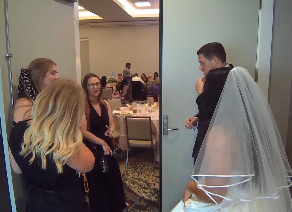 A bride and groom wait behind a door at a wedding reception.