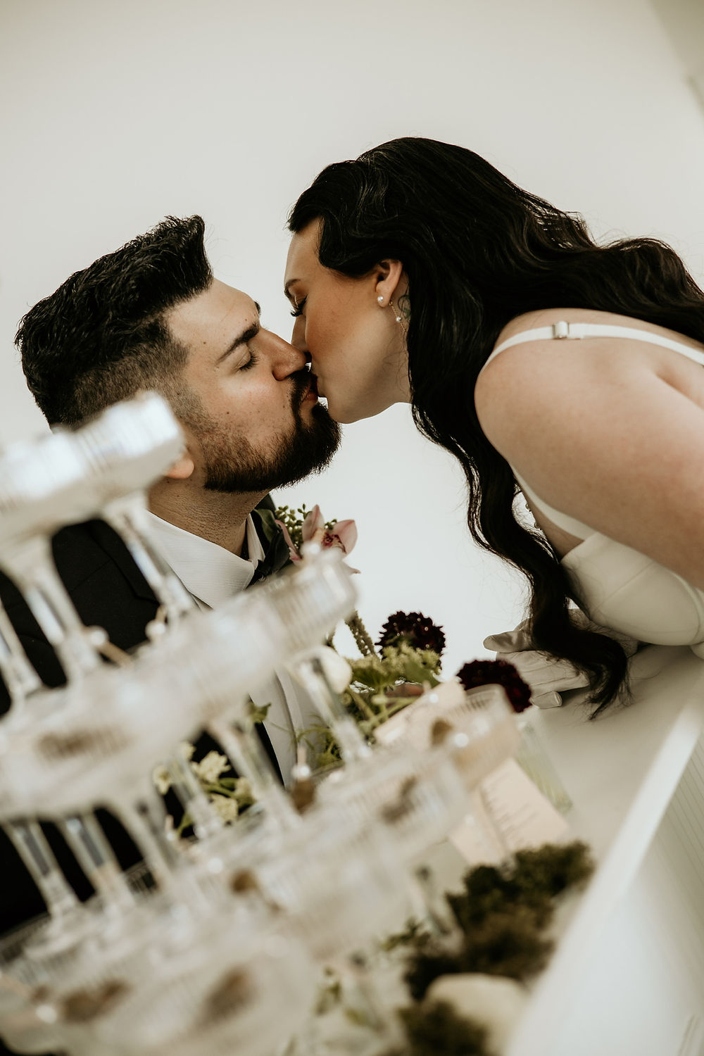 Analea Wedding Co. newlyweds kissing by champagne tower.