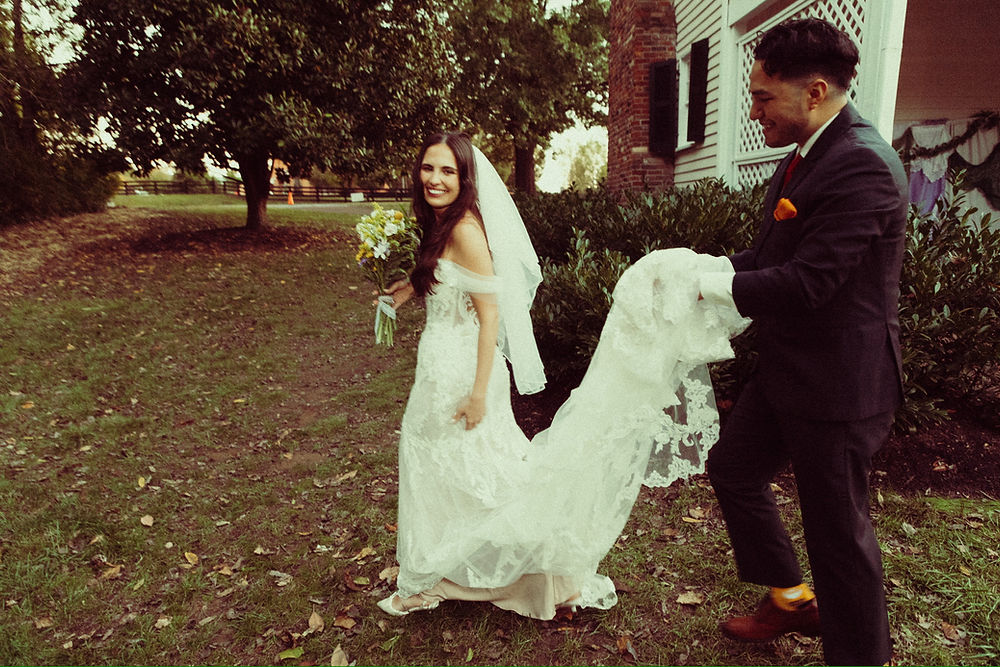 Groom holds train of smiling bride's wedding dress