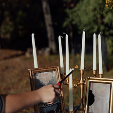 Person lighting white candles in a gold candelabra outdoor.