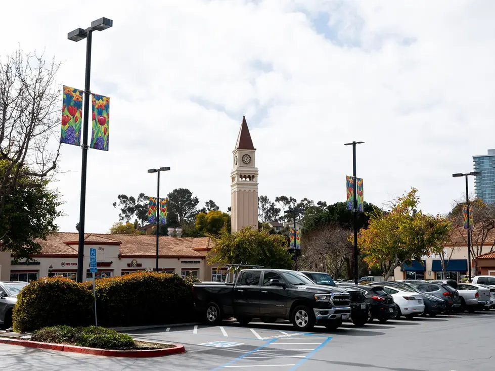 Parking lot with cars, clock tower, and colorful banners.