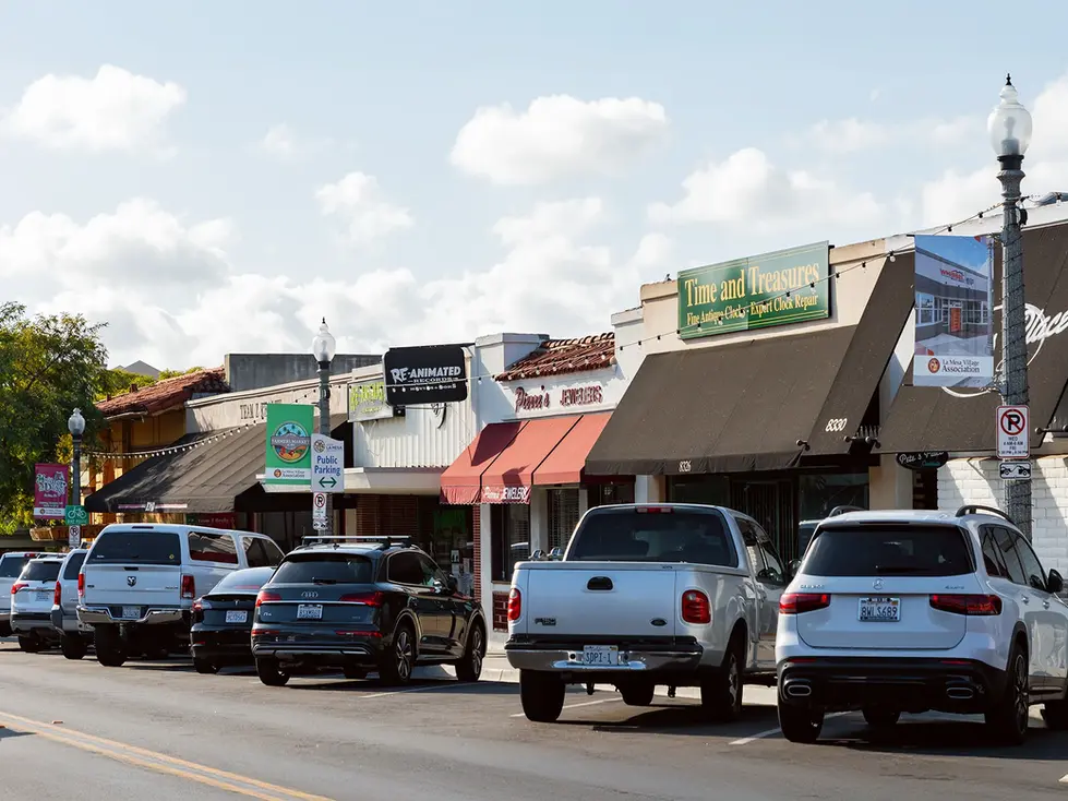 Street with parked cars and various storefronts.