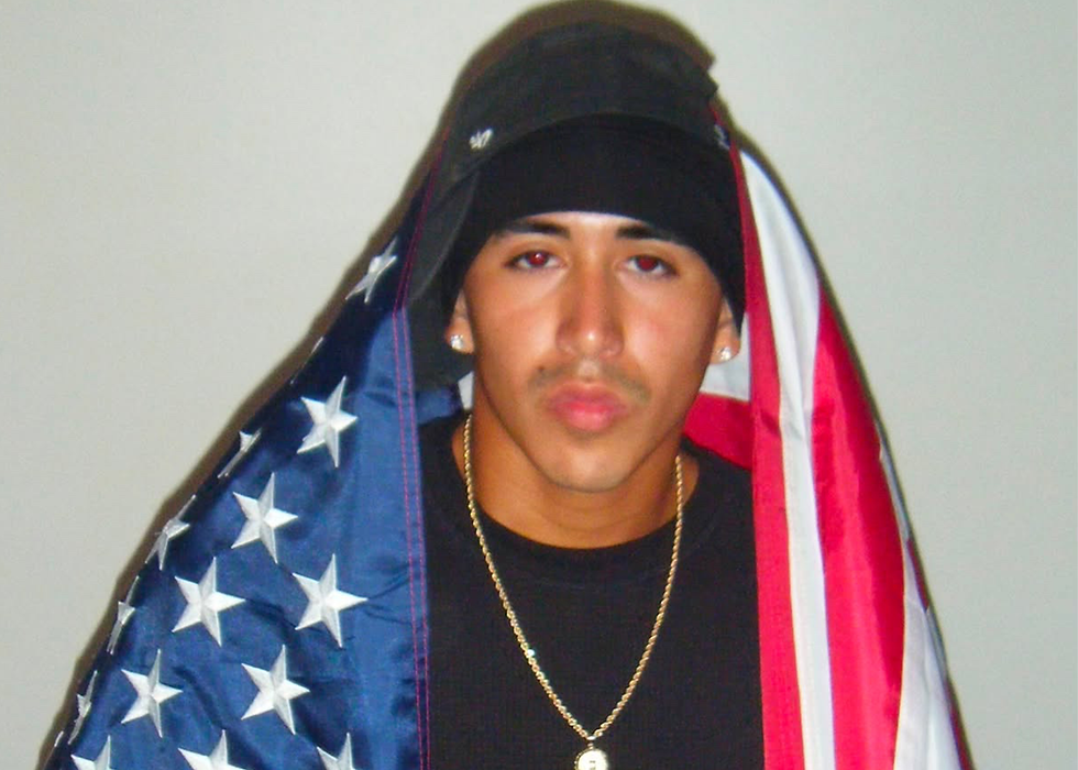 Portrait of independent artist Rico Burgos draped in an American flag during a photoshoot.