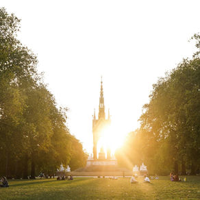 People sit on the grass in Hyde Park in London England at sunset.