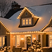 Snow-covered home with classic warm white roofline Christmas lights glowing at night.