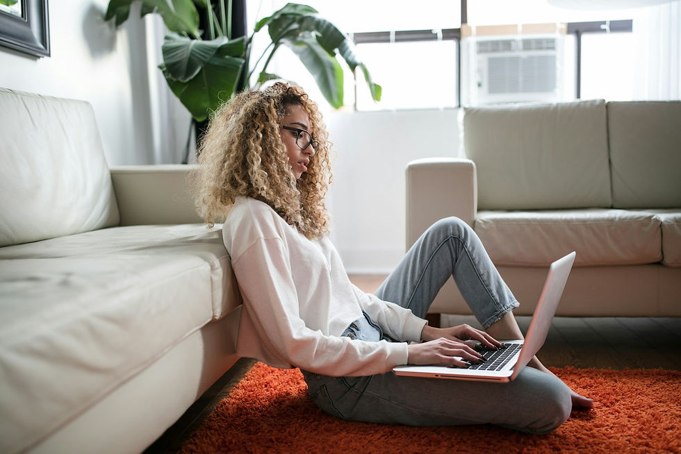 Woman sitting on floor leaning against couch with laptop, representing someone accessing online PTSD therapy from home