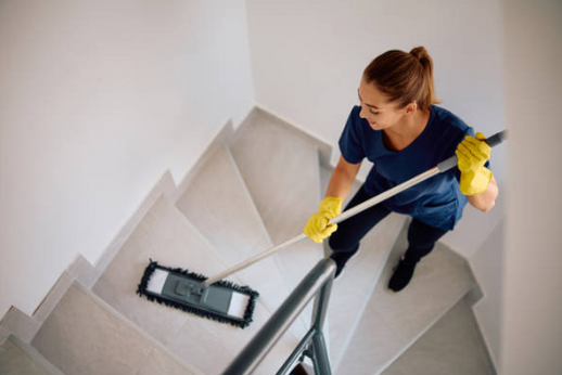 Reinigungskraft wischt eine Treppe im Innenbereich mit Mopp und Eimer.