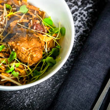 Red pasta with a pork meatball garnished with parmesan cheese, sundried tomato and fresh arugula. Silver utensils and clothe napkin partner it shot by calgary food and beverage photographer