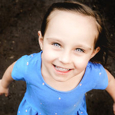 A close up image of a young girl with a blue dress and blue eyes running up to the camera shot by family photographer House of Photography at Bebo Grove Park in Calgary Alberta