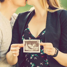 couple kissing while showcasing ultra sound of baby in Carburn park for maternity shoot by calgary family photographer