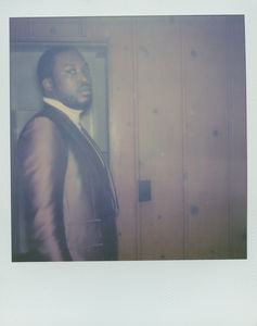 Man in a suit standing against a wood-paneled wall.