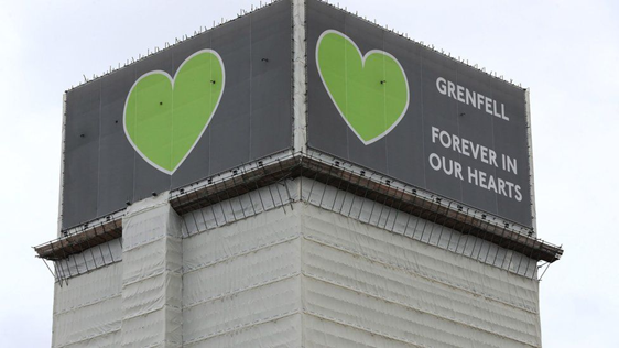 A covered Grenfell tower a banner that reads 'Grenfell, forever in our hearts,' with the iconic green heart symbol.