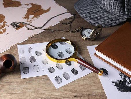 Magnifying glass on fingerprint sheets with notebook, map, pipe, and pocket watch.