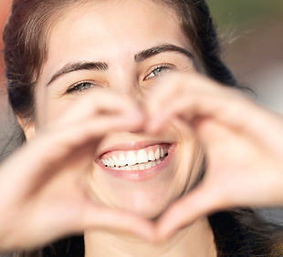 junge Frau, die lächelt und die Hände zu einem Herz formt