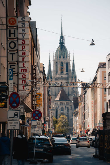 Blick durch eine Münchner Straße mit Hotelschildern auf die neugotische St. Paul Kirche – Streetfotografie München
