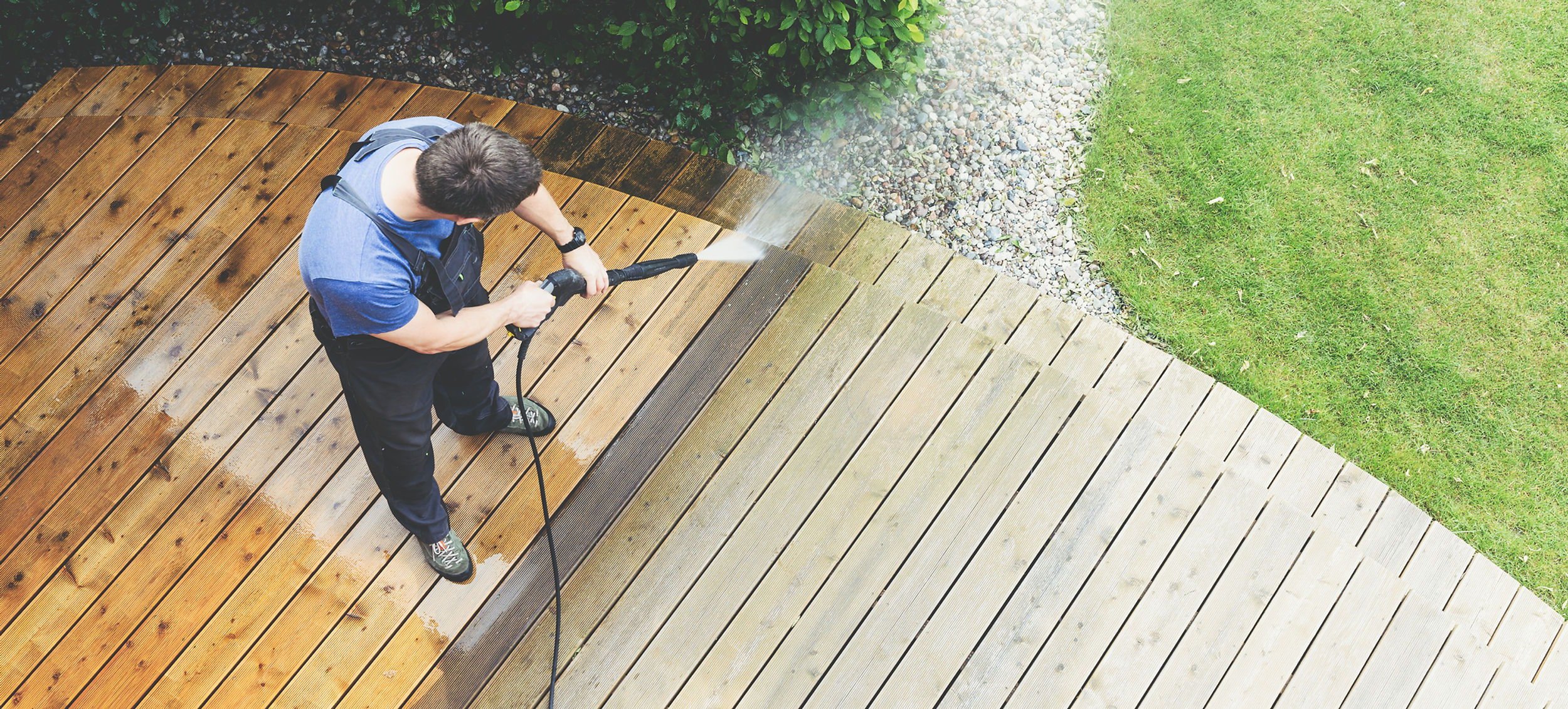 Man using pressure washer to remove dirt and mold from backyard decking.
